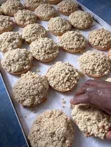 Apple crumble on a tray, with a hand reaching for one of them.