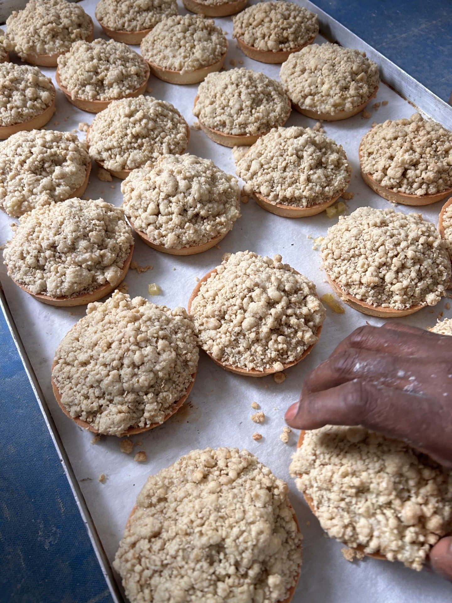 Apple crumble on a tray, with a hand reaching for one of them.