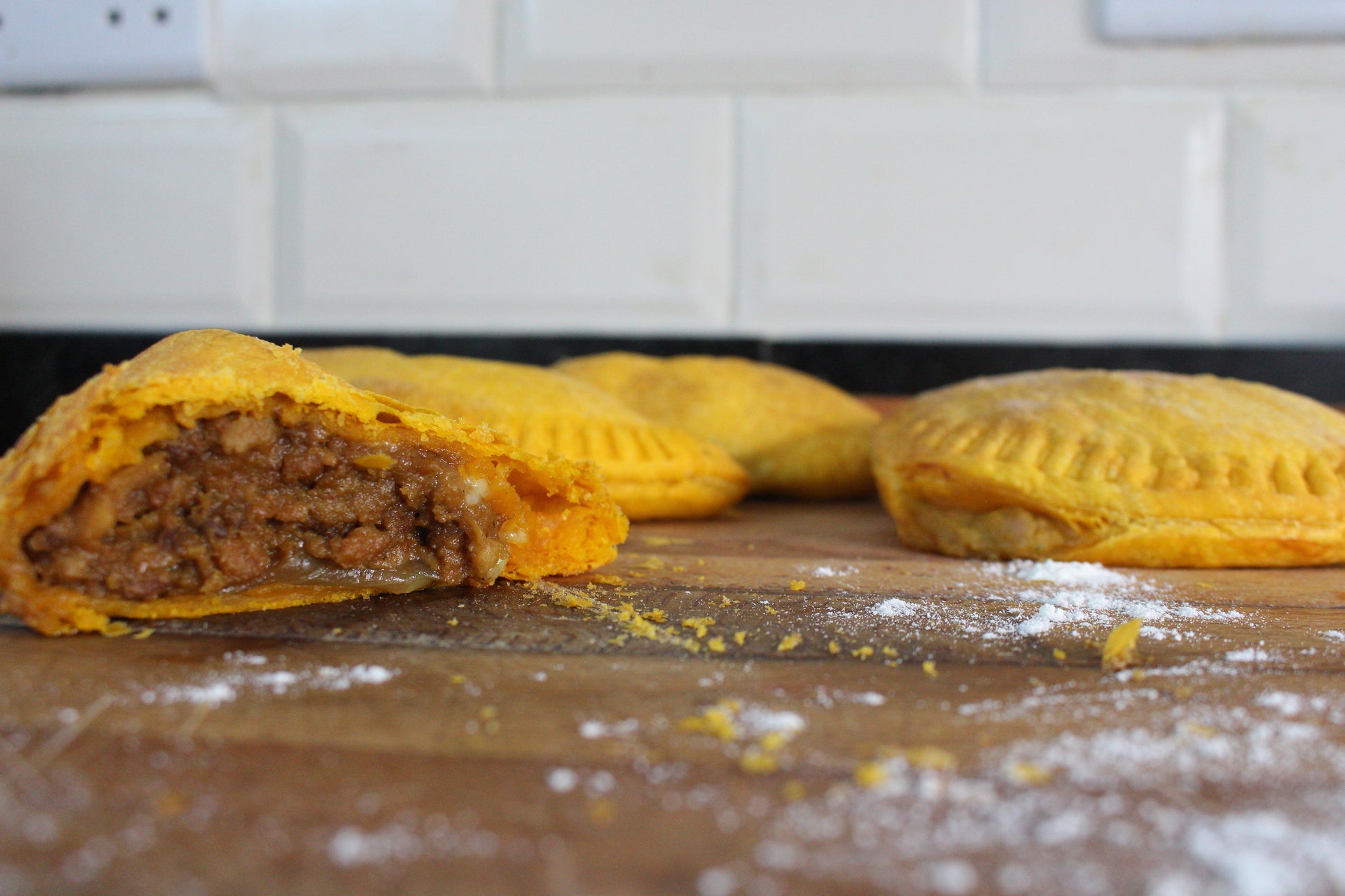 Three beef patties on a wooden board with a tiled wall in the background